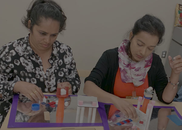 two women building towers over a mirror with random objects