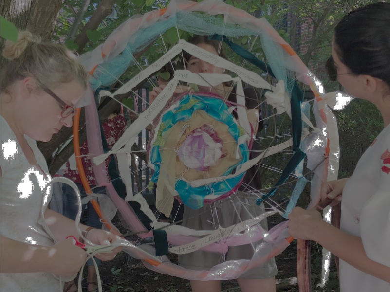 women weaving a hoop with random strips of ribbon